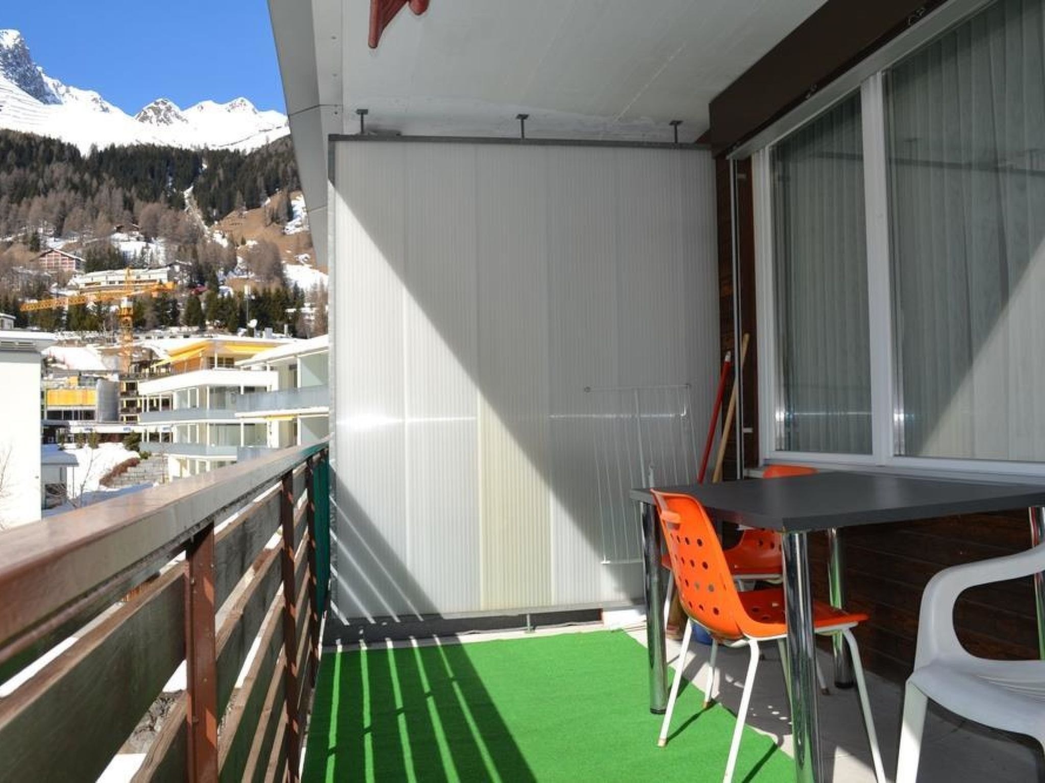 A balcony with a table and chairs, a view of a snowy mountain range, and a green artificial turf floor.