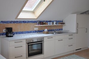 A kitchen with a skylight, white cabinets, a stove, and a coffee maker. - Charming holiday apartment 3 (Salem)