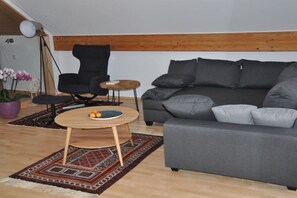 A living room with a grey sofa, a black armchair, a small wooden table with fruit, and a patterned rug. - Charming holiday apartment 3 (Salem)