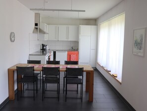 Ett modernt kök med vita skåp, ett träbord med fyra stolar och ett fönster med vita gardiner.