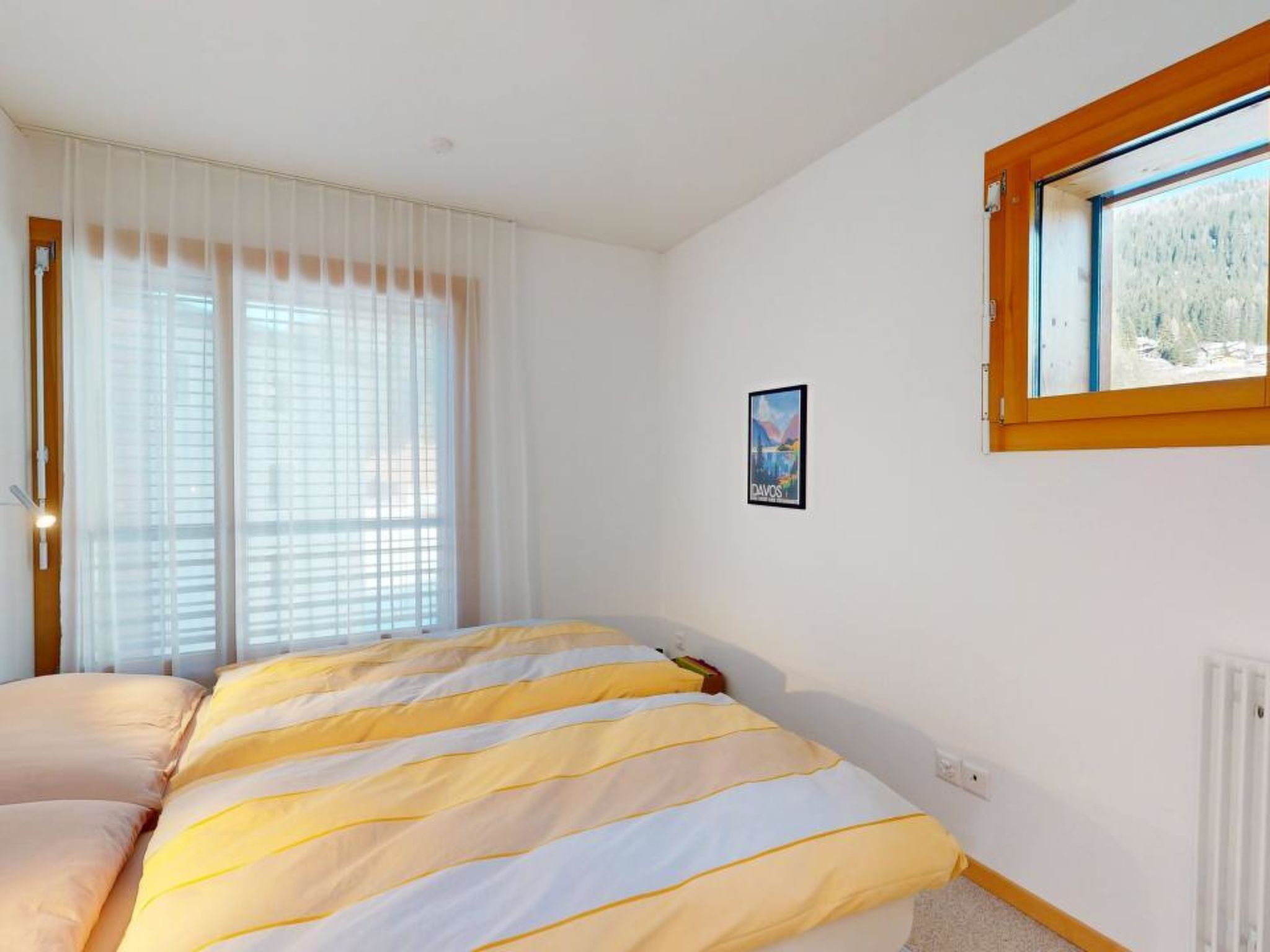 A bedroom with a bed, a window with a view, and a poster on the wall.