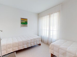 A bedroom with two single beds, a poster on the wall, and a window with sheer curtains. - am Dischmabach D Appartement/Fewo, Dusche oder Bad, WC 3½-Zimmerwohnung by Interhome (Davos)