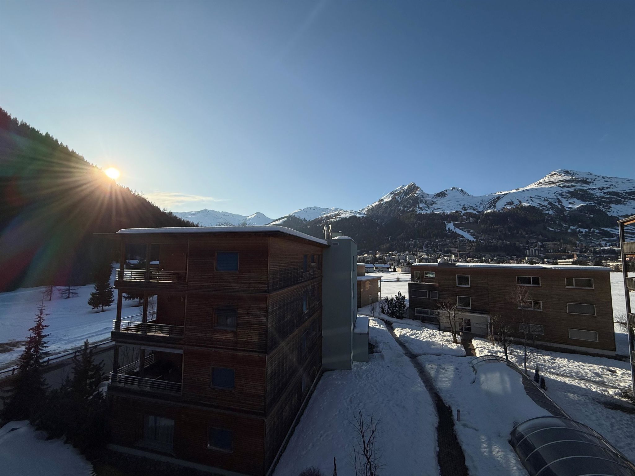 A multi-story building with a flat roof, surrounded by snow-covered ground and mountains in the background.