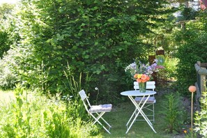 Ein Sitzbereich im Freien mit Tisch und Stühlen, umgeben von üppiger Bepflanzung und einer dichten Hecke.