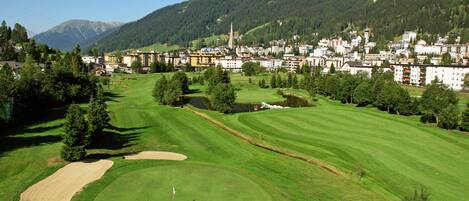 A golf course with a flagstick, surrounded by a residential area with houses and a church.