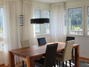 A dining area with a wooden table and chairs, large windows with curtains, and a hanging light fixture. - Talstrasse 57E (RA) Appartement/Fewo, Dusche oder Bad, WC 4½-Zimmerwohnung by Interhome (Davos)