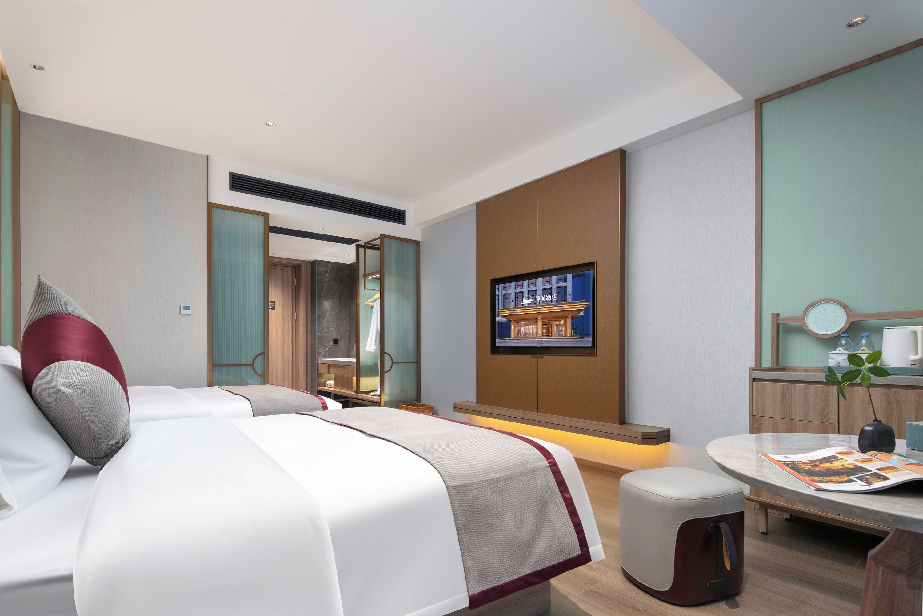 A modern hotel room with a large bed, a desk, a chair, a small table, and a television mounted on the wall.