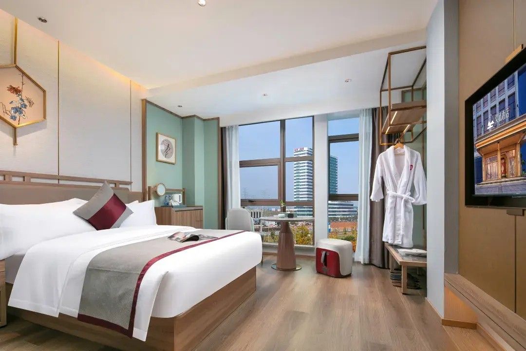 Habitació d'hotel amb un llit, una televisió, una finestra amb vista a la ciutat i un penjador per a robes.