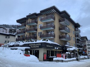A multi-story building with balconies, a restaurant named 'RISTORANTE PADRINO' on the ground floor, and snow on the roof and ground. - Quellenhof C01 Appartement/Fewo, Dusche oder Bad, WC 3½-Zimmerwohnung by Interhome (Davos)