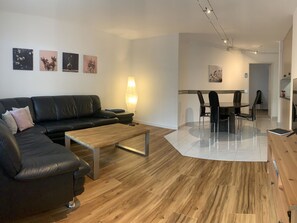 A modern living room with a black leather sofa, a wooden coffee table, and a dining area with a glass table and chairs. - Quellenhof C01 Appartement/Fewo, Dusche oder Bad, WC 3½-Zimmerwohnung by Interhome (Davos)
