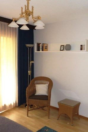 A room with a wicker chair, a small table, a floor lamp, and a ceiling light fixture. - Carlton am Golf C14 Appartement/Fewo, Dusche oder Bad, WC 2-Zimmerwohnung by Interhome (Davos)
