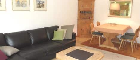 Uma sala de estar com sofá preto, mesa de centro de madeira, mesa de jantar com cadeiras e um armário.