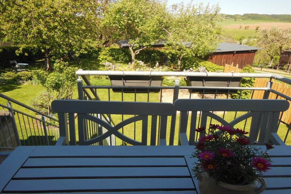 A balcony with a view of a green landscape, a wooden fence, and a table with a potted plant.
