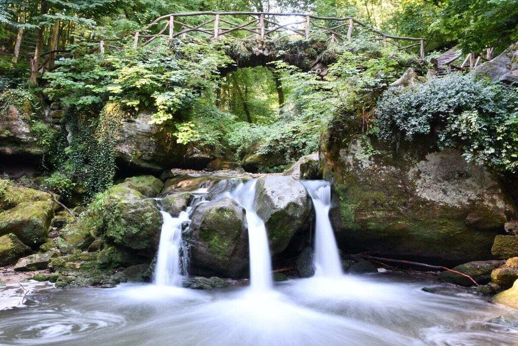 A natural waterfall with a wooden bridge above it.