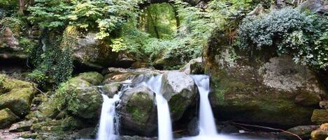 A natural waterfall with a wooden bridge above it.