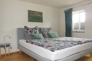 A bedroom with a bed, a small table, a window with curtains, and a painting on the wall. - Holiday apartment with 2 bedrooms (Holsthum)