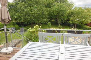 A deck with a white railing, a beige umbrella, and lush greenery in the background. - Holiday apartment with 2 bedrooms (Holsthum)