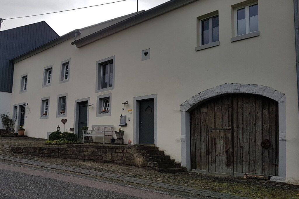 Ein zweistöckiges Gebäude mit einem steinernen Rundbogenportal, einer kleinen Veranda mit einer Bank und einer Reihe von Fenstern.