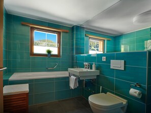 A bathroom with a bathtub, sink, and toilet, all with teal tiles. - Haus Rätia App 16 Appartement/Fewo, Dusche oder Bad, WC 2½-Zimmerwohnung by Interhome (Klosters)
