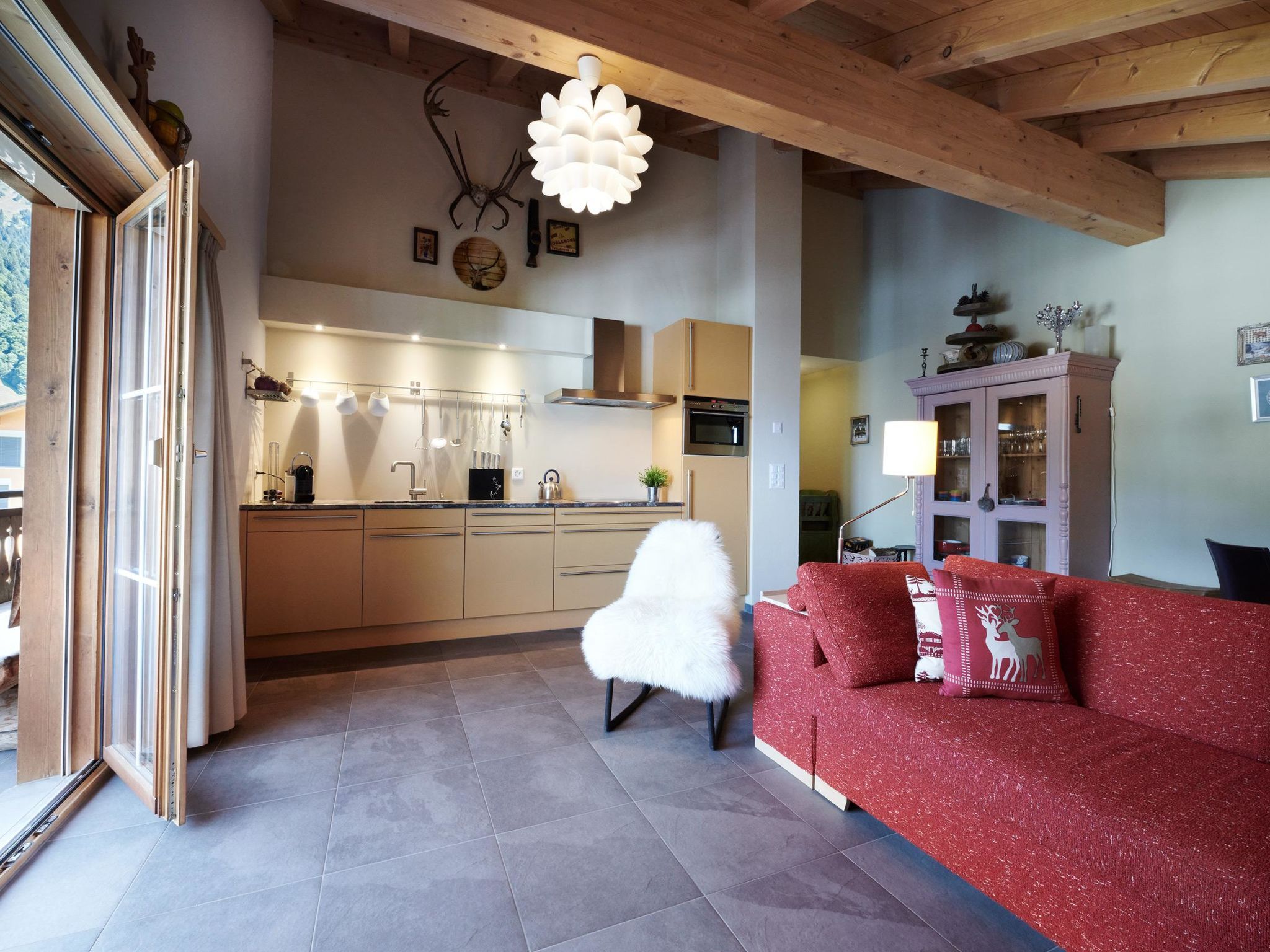 Una cocina moderna con una isla central, un sofá rojo con almohadas de reno y una butaca blanca y mullida.