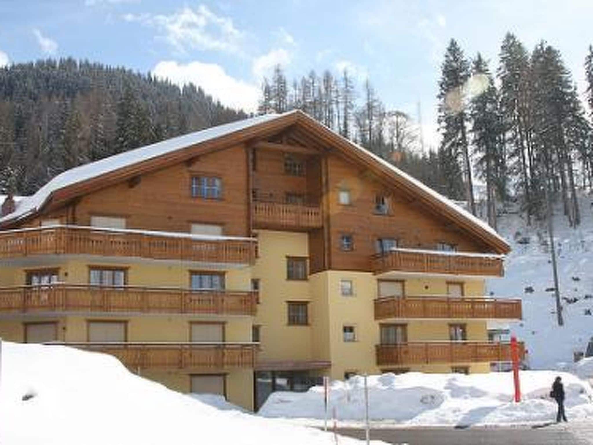 A multi-story wooden building with balconies, surrounded by snow and trees.