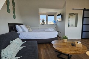 A modern bedroom with a bed, a sofa, a round wooden table, and a window with a view. - Holiday apartment with 1 bedroom (Zandvoort)