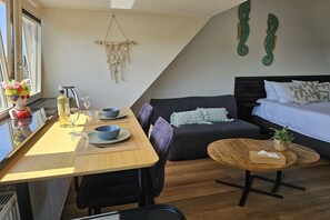 A compact living space with a dining area, a sofa, a bed, and a small round table. - Holiday apartment with 1 bedroom (Zandvoort)