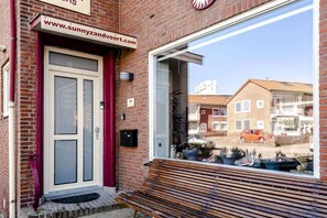 A brick building with a red door and a bench outside. - Holiday apartment with 1 bedroom (Zandvoort)