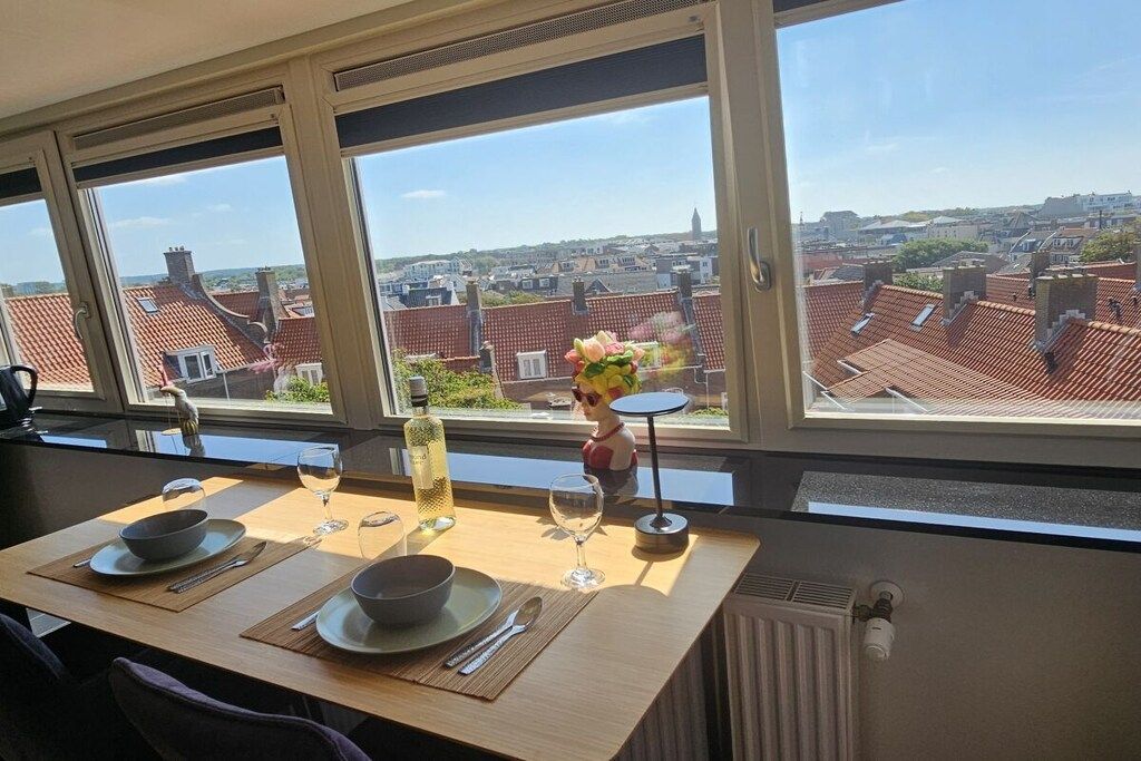 A dining area with a table set for two, a vase with flowers, and a bottle of liquor.