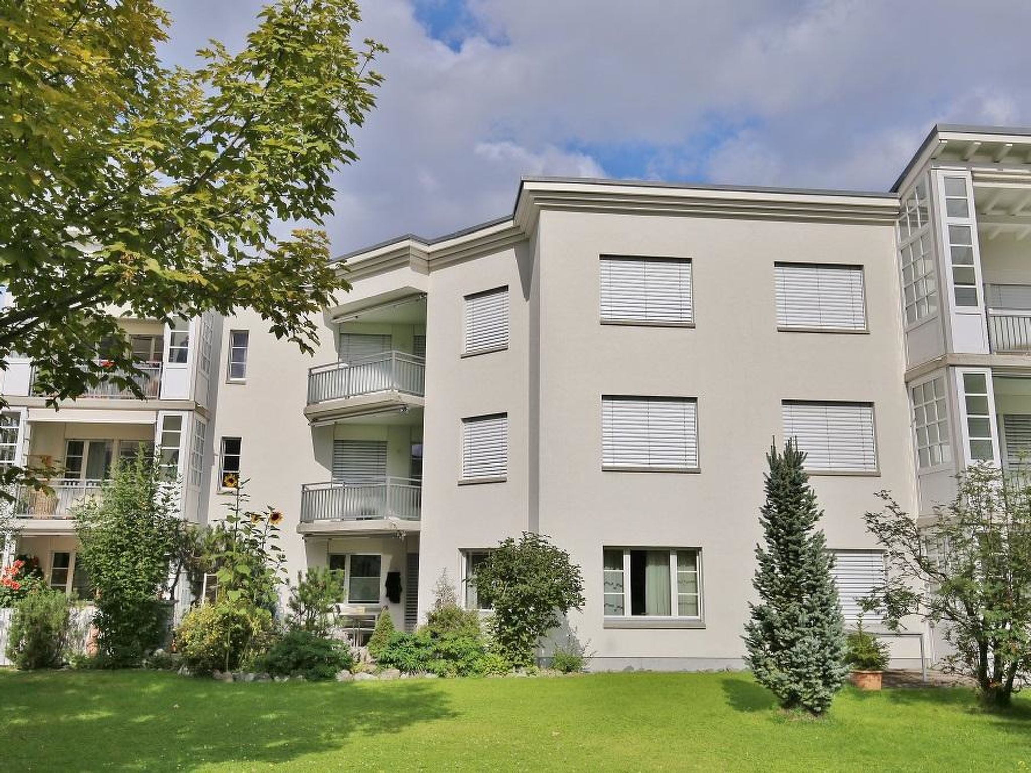 A multi-story residential building with balconies, large windows, and a well-maintained lawn.