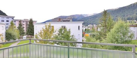 Un balcon doté d’un sol en gazon synthétique vert, donnant sur un quartier résidentiel avec des immeubles et une montagne en arrière-plan.