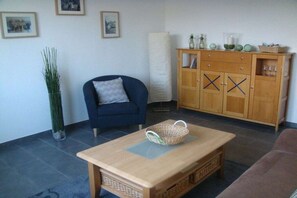 Ein Wohnzimmer mit einer Couch, einem Couchtisch, einem Schrank und einer hohen Pflanze.