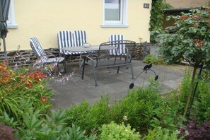 Eine Terrasse mit Tisch und Stühlen, umgeben von Pflanzen und einer gelben Wand.
