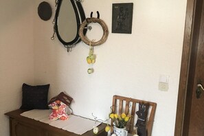 A room with a mirror, a wall-mounted decoration, a small table with a cushion, a chair with a vase of flowers, and a door. - Holiday apartment with 1 bedroom (Oberhausen)
