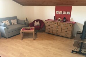 A living room with a grey sofa, a red armchair, a wooden dresser, and a small table. - Holiday apartment with 1 bedroom (Oberhausen)