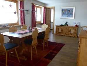 Ein Essbereich mit einem Holztisch, Stühlen und einem roten Teppich. Ein Schrank mit Dekorationsgegenständen und ein Gemälde an der Wand sind ebenfalls vorhanden.
