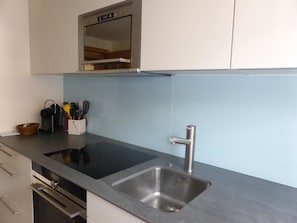 Cozinha com pia de aço inoxidável, forno embutido e bancada com cesta de utensílios.