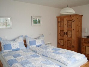Ein Schlafzimmer mit einem Doppelbett, einem Holzschrank, einem gerahmten Bild an der Wand und einer Pendelleuchte.