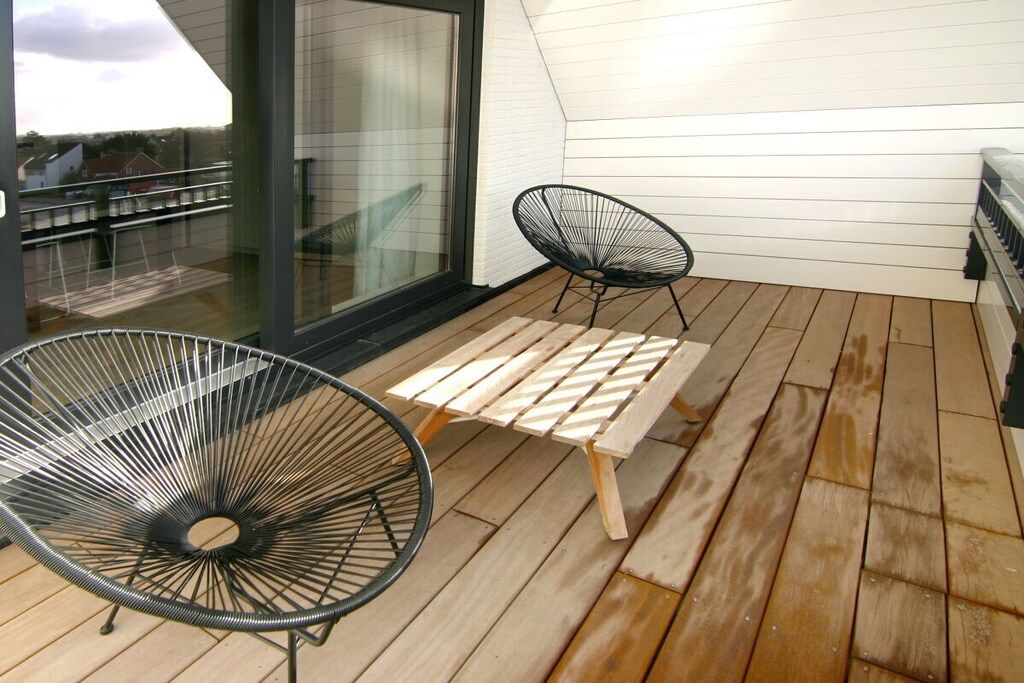 Une terrasse en bois avec deux chaises en fil de fer noir et une table en bois.