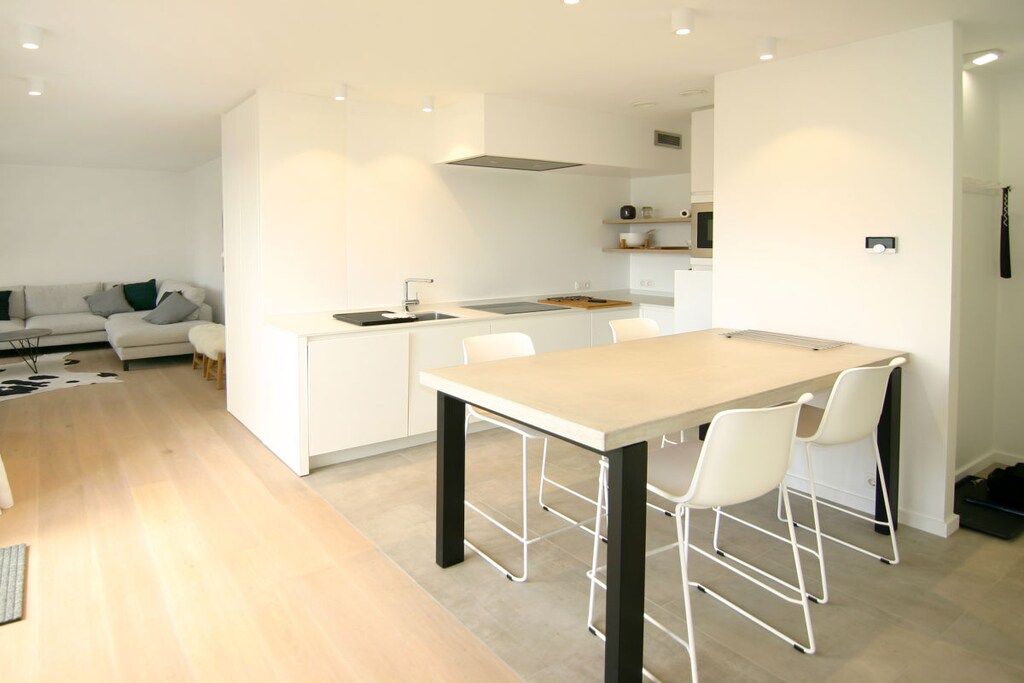 A modern kitchen with a central island, white cabinetry, and a dining area with chairs.