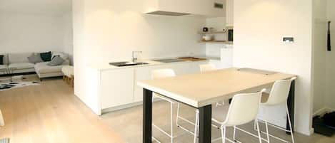 A modern kitchen with a central island, white cabinetry, and a dining area with chairs.