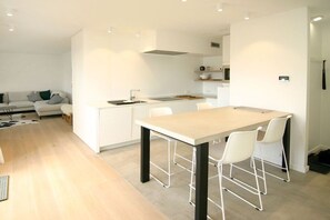 Een moderne keuken met een centraal eiland, witte kastjes en een eethoek met stoelen.