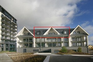 A multi-story residential building with balconies, a parking area, and a landscaped front yard. - Beach Residence A305 (Cadzand)
