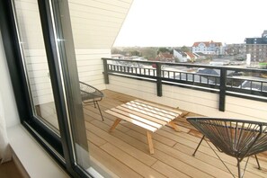 A balcony with a wooden table and two chairs, a view of buildings in the background. - Beach Residence A305 (Cadzand)