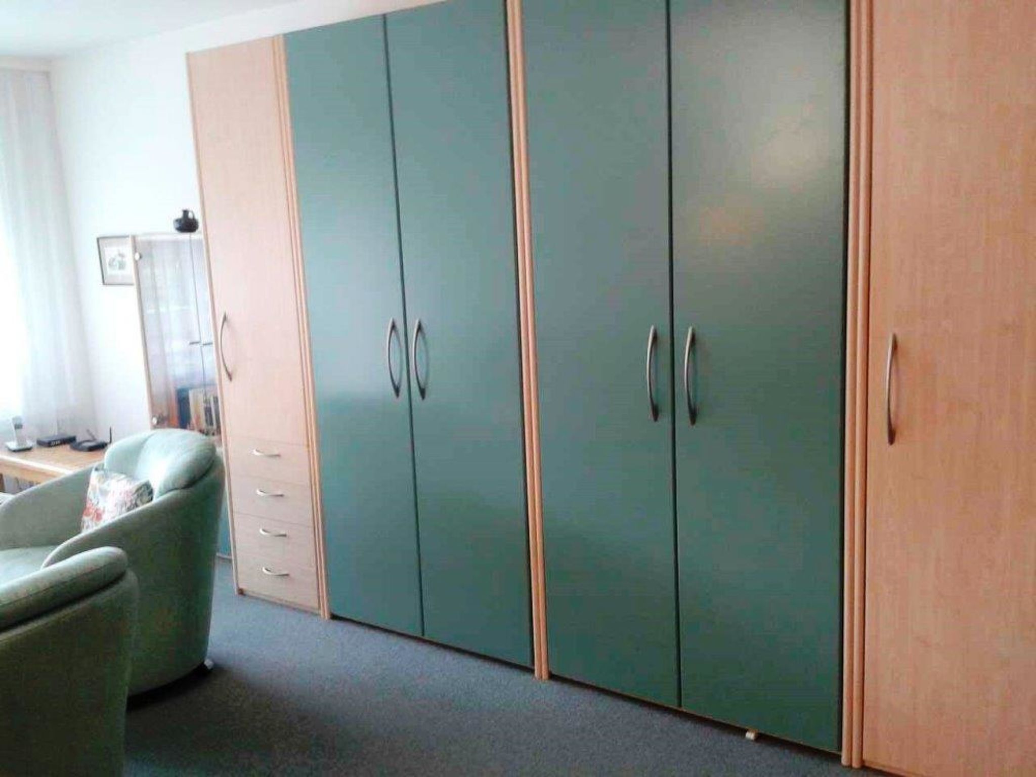 Ein Zimmer mit großem Kleiderschrank, einem Sessel und einem Schreibtisch mit Lampe.
