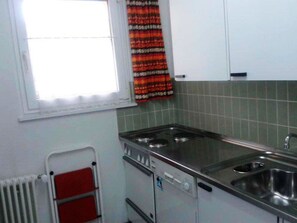 A compact kitchen with a stove, sink, and a window with a curtain. - Hertisun 7 Appartement/Fewo, Dusche oder Bad, WC 2½-Zimmerwohnung by Interhome (Davos)