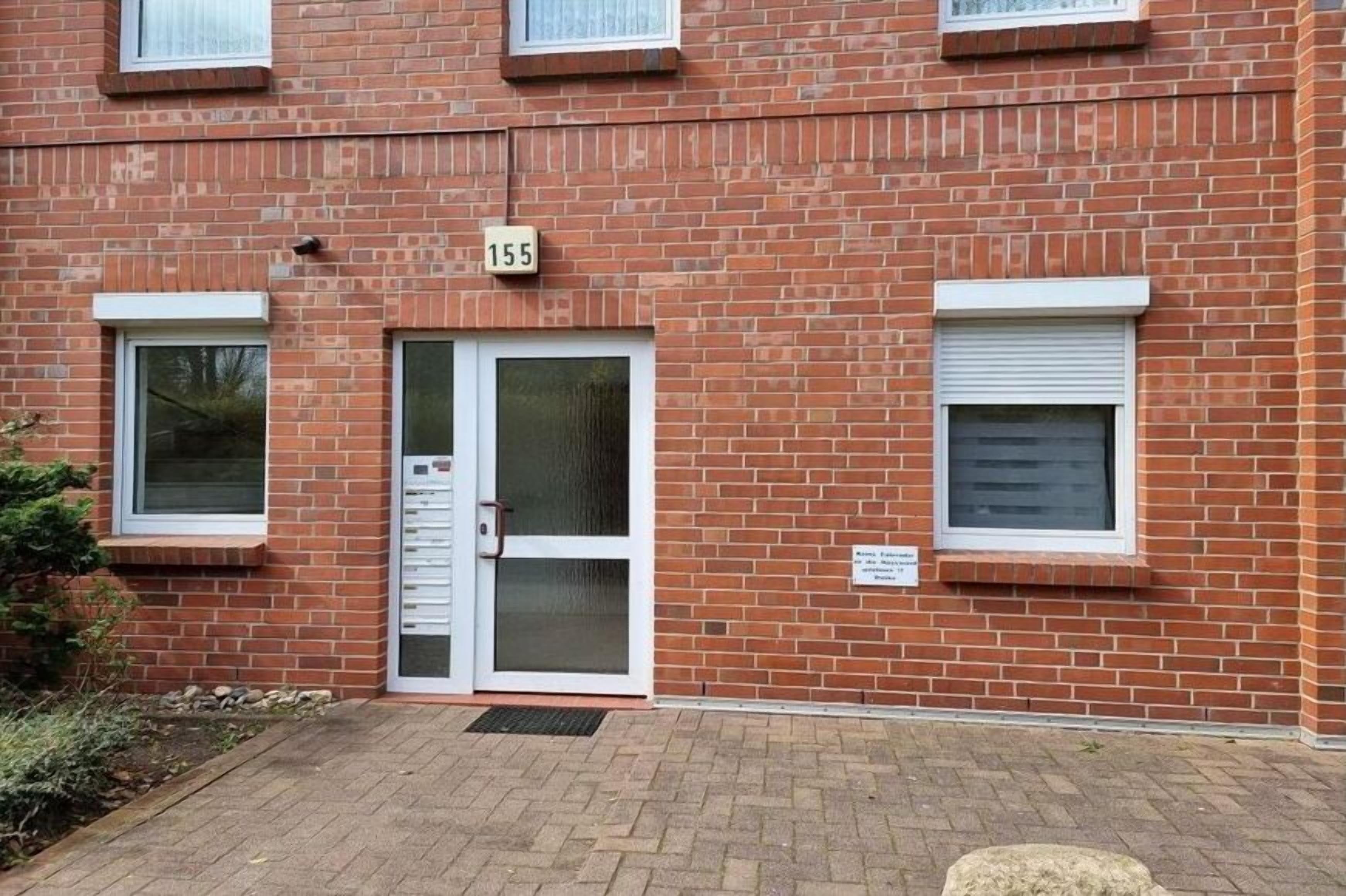 Ein rot backsteiner Gebäude mit einer nummerierten Tür, einem Fenster mit Rollo und einem kleinen Schild an der Wand.