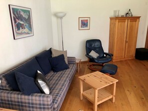 Un salon avec un canapé à carreaux, un fauteuil en cuir noir, une table basse en bois et un meuble en bois.