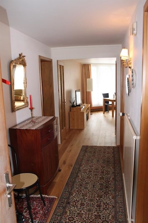Un couloir avec un plancher en bois, un tapis à motifs, un miroir, une commode et une chaise.