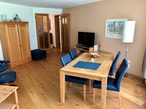 Ein Essbereich mit Holztisch und blauen Stühlen, einem Fernseher auf einem Schrank und einem Schrank mit Glastür.